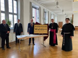 Vertreter von Erzbistum und Stadt Walldürn mit dem Walldürner Ortsschild und dem Namenszusatz Wallfahrtsstadt