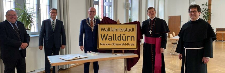 Vertreter von Erzbistum und Stadt Walldürn mit dem Walldürner Ortsschild und dem Namenszusatz Wallfahrtsstadt
